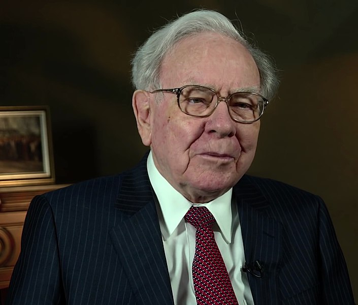 Warren Buffet. Ele é um homem idoso, branco, de cabelos brancos e óculos e que veste terno escuro com camisa branca e gravata vermelha. Ele disse que não tem interesse em investir em cirptomoedas