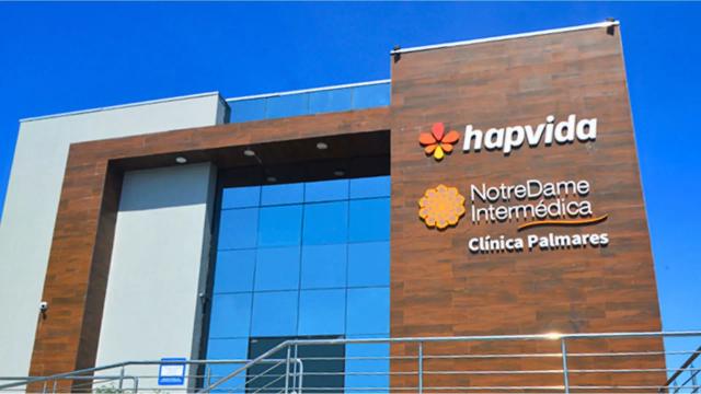 Fachada da unidade Hapvida sob céu azul, com a marca e slogan visíveis.