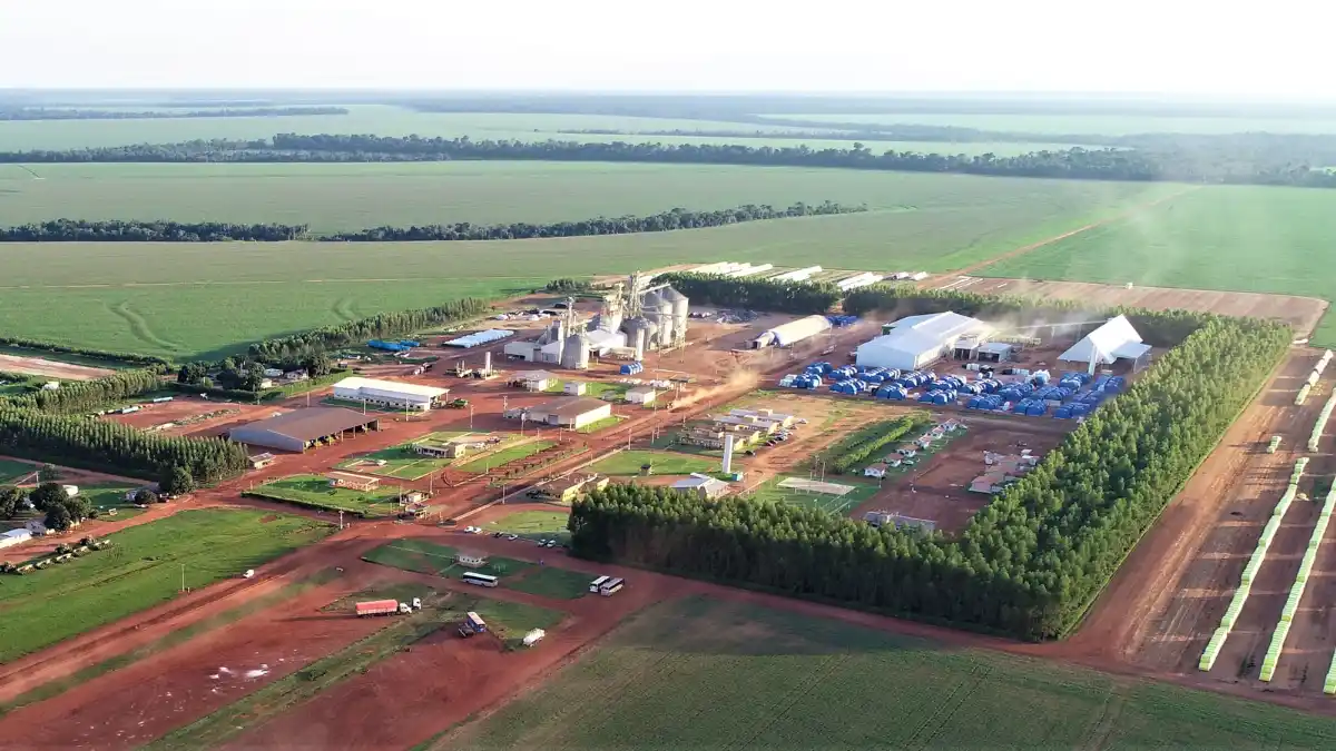 Vista aérea de uma grande fazenda da SLC Agrícola, mostrando a estrutura de armazenamento (silos) no centro e extensas plantações em volta.
