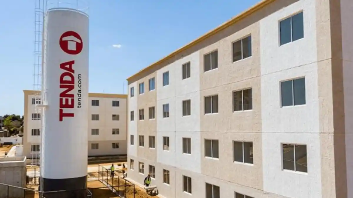 Vista de um condomínio popular com blocos de apartamentos e a caixa d'água cilíndrica com o logo da Tenda em destaque, representando a construtora.