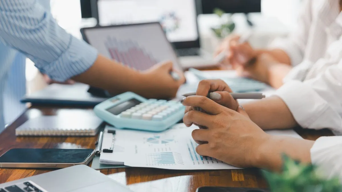 Mãos sobre uma calculadora e documentos financeiros, simbolizando o cálculo do Imposto de Renda sobre investimentos em ações.
