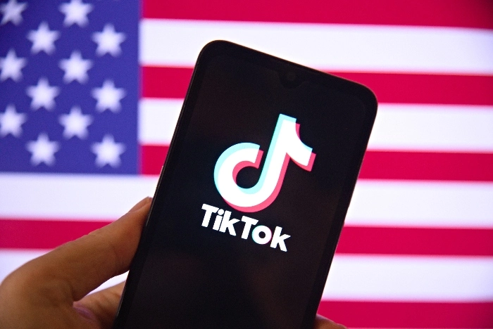 TikTok no celular e bandeira dos EUA ao fundo