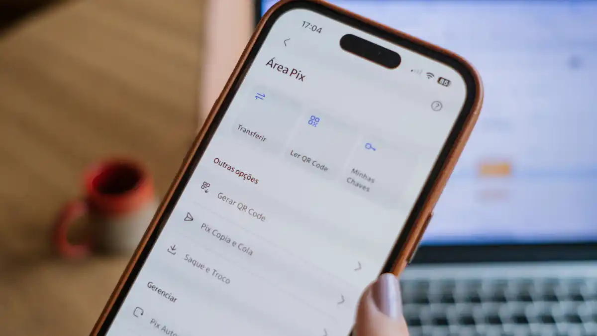 Mão segurando um smartphone que mostra a interface de pagamentos de um aplicativo financeiro, ilustrando a evolução das transações digitais (Pix).