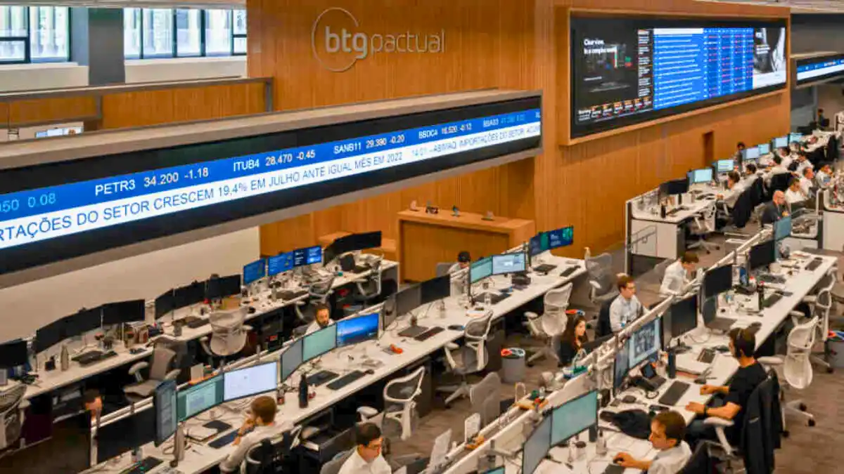 Visão ampla do trading floor do BTG Pactual, com múltiplos monitores de cotações, simbolizando o lucro recorde do 3º trimestre de 2025.