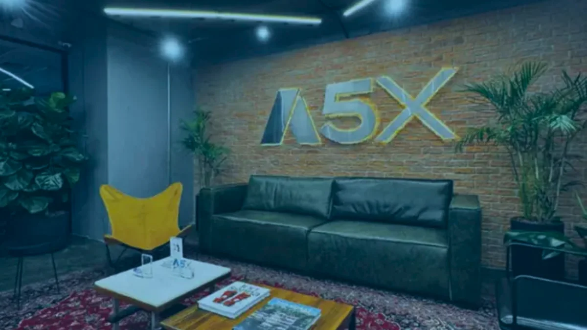 Ambiente de escritório moderno com um grande logotipo da A5X iluminado em dourado em uma parede de tijolos, simbolizando a nova bolsa de derivativos do Brasil.