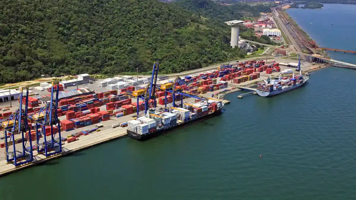 Vista aérea de um grande porto com navios atracados e pilhas de contêineres coloridos, simbolizando os ativos de logística e infraestrutura que a CSN planeja cindir.