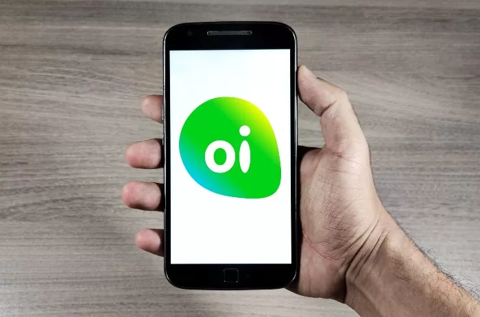 Falência da Oi é suspensa: mão segura celular com logo da companhia