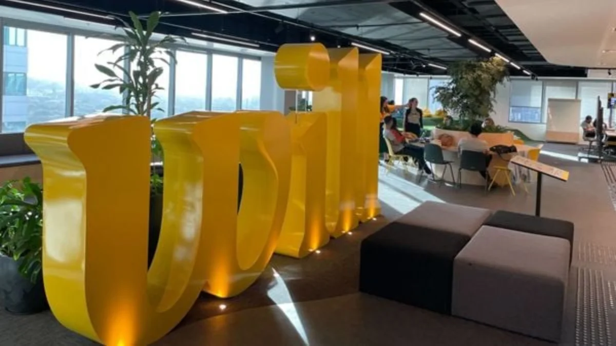 Grande letreiro amarelo e tridimensional com a palavra Will em um escritório moderno e iluminado, representando o Will Bank em meio à análise de liquidação.