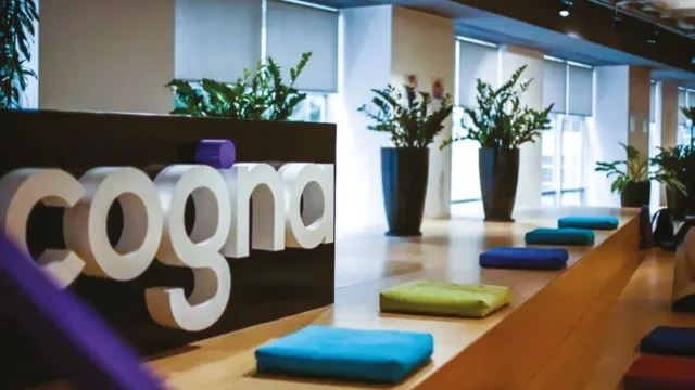 Vista interna de um campus da Cogna com alunos sentados em mesas de estudo em um ambiente moderno e colorido, com o logotipo da Kroton ao fundo, representando os resultados da cogna 4t25.