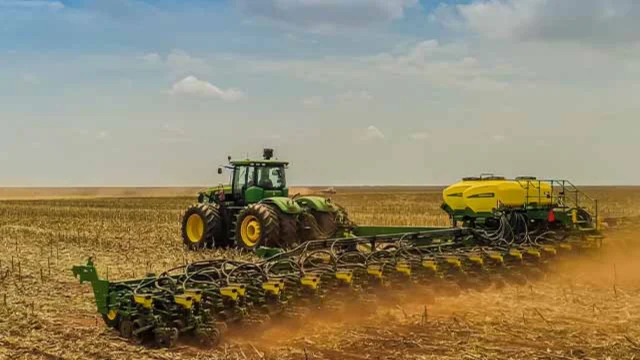 Trator verde de grande porte operando uma plantadeira amarela em um vasto campo agrícola sob céu nublado, ilustrando a tecnologia no campo e os resultados da Vittia 4t25.