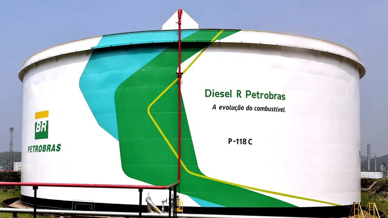 Vista frontal de um grande tanque de armazenamento cilíndrico e branco da Petrobras em uma refinaria. O tanque exibe o logotipo da Petrobras (BR) à esquerda e a inscrição "Diesel R Petrobras - A evolução do combustível" ao centro, acompanhada da identificação técnica "P-118 C". Grafismos em tons de verde e azul decoram a lateral, e tubulações vermelhas de segurança são visíveis na parte superior e frontal.