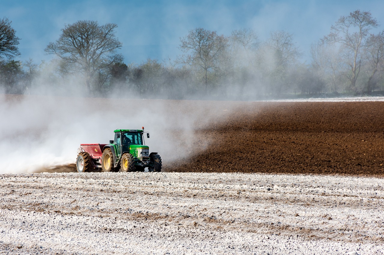 Imagem mostra um trator aplicando fertilizante na lavoura.