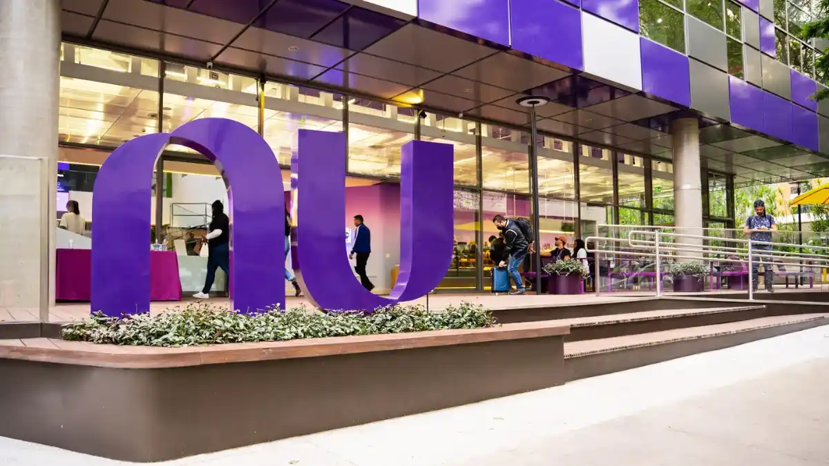 Fachada do escritório do Nubank com o grande logotipo roxo "Nu" em destaque, simbolizando a busca da fintech pela licença para virar banco a partir de 2026.