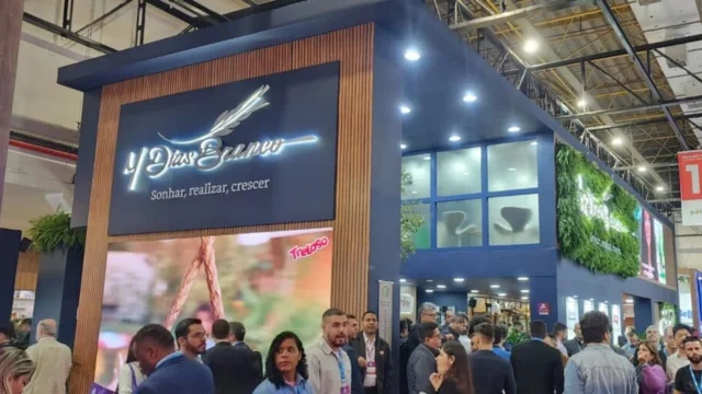 Estande moderno da M. Dias Branco em uma feira de alimentos, com o logotipo iluminado e o slogan "Sonhar, realizar, crescer" em destaque, cercado por visitantes, representando a m. dias.