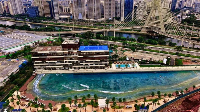 Vista aérea do complexo SP Surf Club FII em São Paulo, destacando a piscina de ondas artificiais, o clube social e a Ponte Estaiada ao fundo.