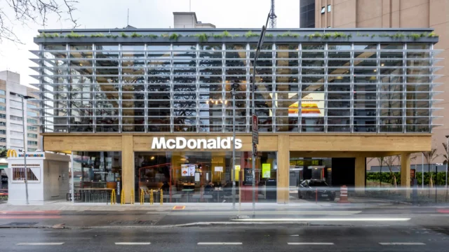 Fachada de uma unidade moderna do McDonald’s operada pela Arcos Dorados, com estrutura de madeira clara, amplas janelas de vidro e brises horizontais, ilustrando a presença da marca para análise da Arcos Dorados.