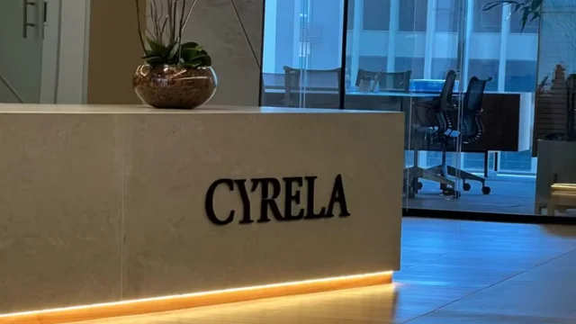 Balcão de recepção moderno em mármore cinza com o logotipo da Cyrela em letras pretas e iluminação de LED na base, representando a sede da empresa para os resultados da Cyrela 4T25.