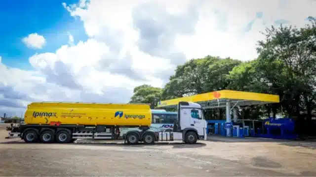 Caminhão-tanque branco e amarelo da Ipiranga com a marca Ipimax estacionado em um posto de combustível sob céu nublado, ilustrando a operação da Ultrapar Ipiranga.