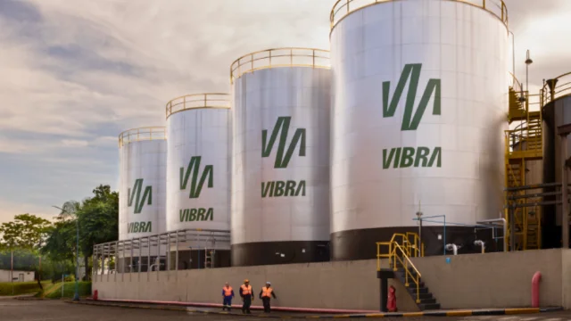 Fileira de grandes tanques metálicos de armazenamento de combustível com o logotipo verde da Vibra, ilustrando a infraestrutura que sustenta os vibra ventos favoráveis no setor de distribuição.