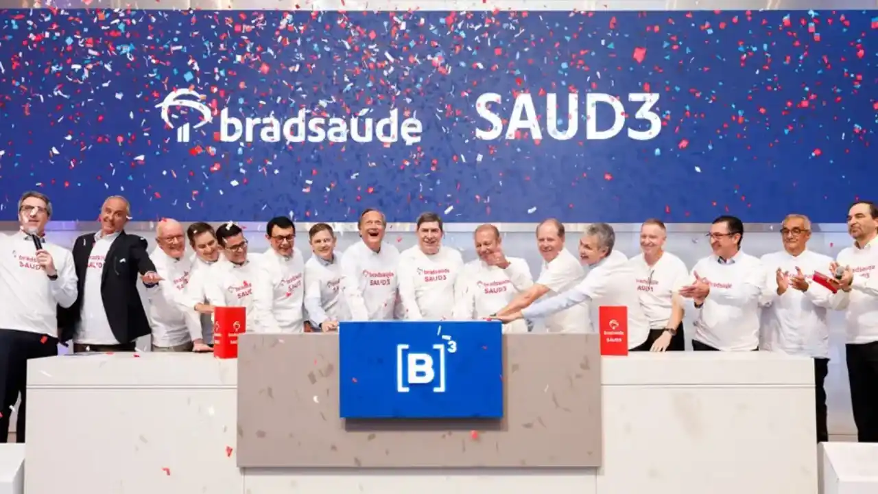 Cerimônia de toque de campainha na bolsa de valores brasileira, B3. No centro, um grupo de executivos e conselheiros homens, vestindo camisetas brancas com o logotipo "bradsaúde SAUD3", comemoram com sorrisos e aplausos. Ao fundo, um grande painel azul exibe as marcas Bradsaúde e o ticker SAUD3 sob uma chuva de confetes vermelhos, brancos e azuis. À frente, o balcão com o logotipo azul da B3.