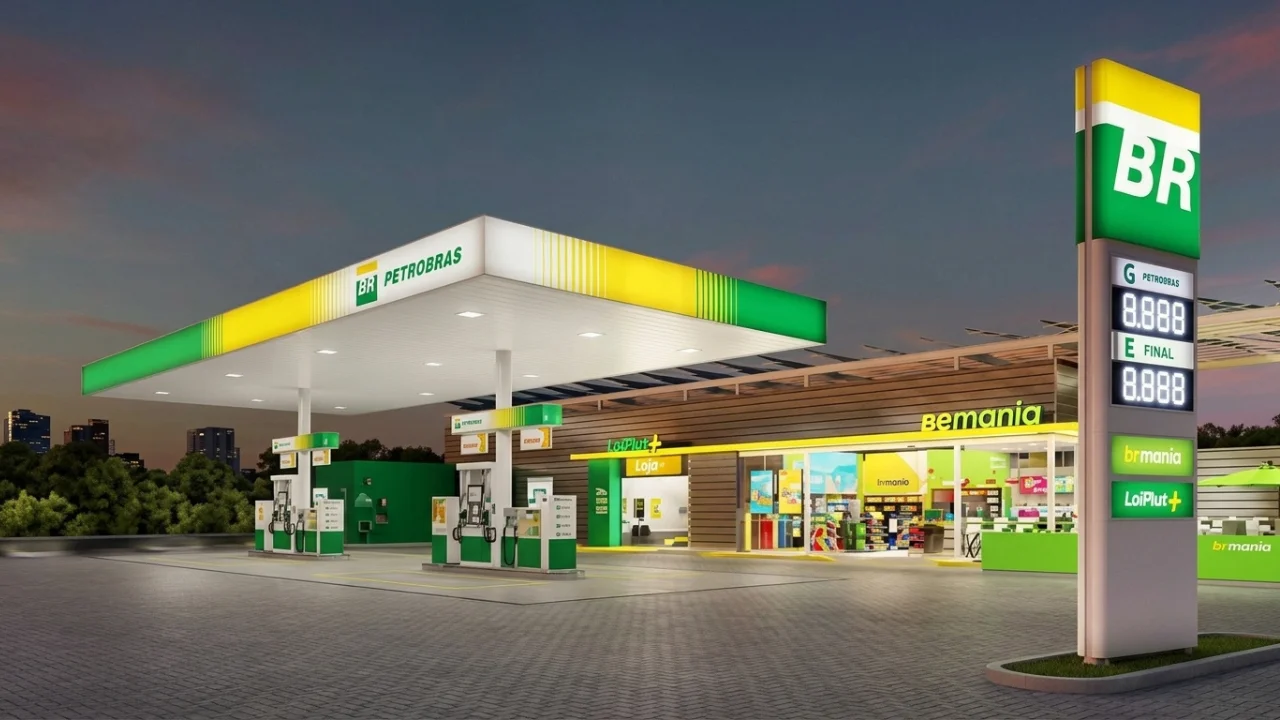 Vista em perspectiva de um posto de combustíveis da Petrobras em um dia ensolarado. Em destaque, a testeira do posto com as cores verde e amarelo e o logotipo da Petrobras. Abaixo, as bombas de combustível estão organizadas, com um carro branco sendo abastecido. Ao fundo, o céu azul com poucas nuvens e árvores completam a cena urbana.