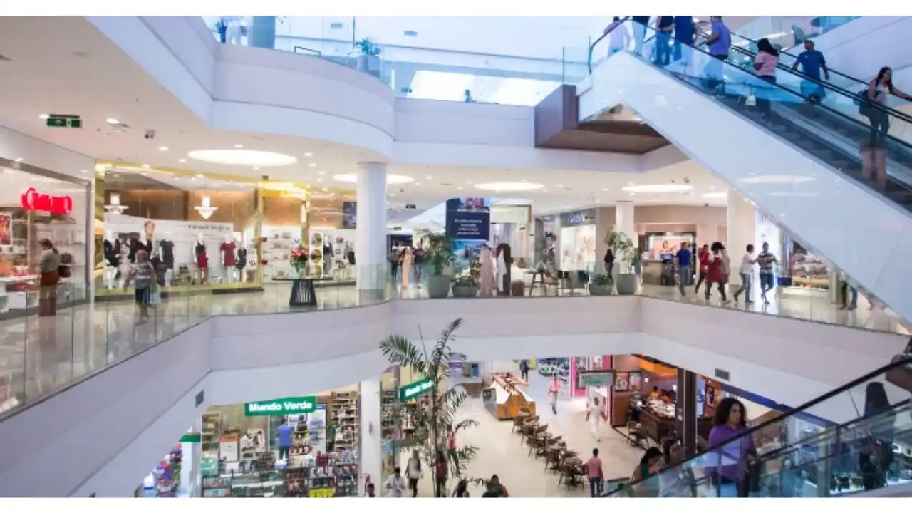 Shopping administrado pela Allos (ALOS3), que divulgou os resultados do 2T26, com átrio amplo iluminado, escadas rolantes em movimento com visitantes e lojas nos diversos andares.
