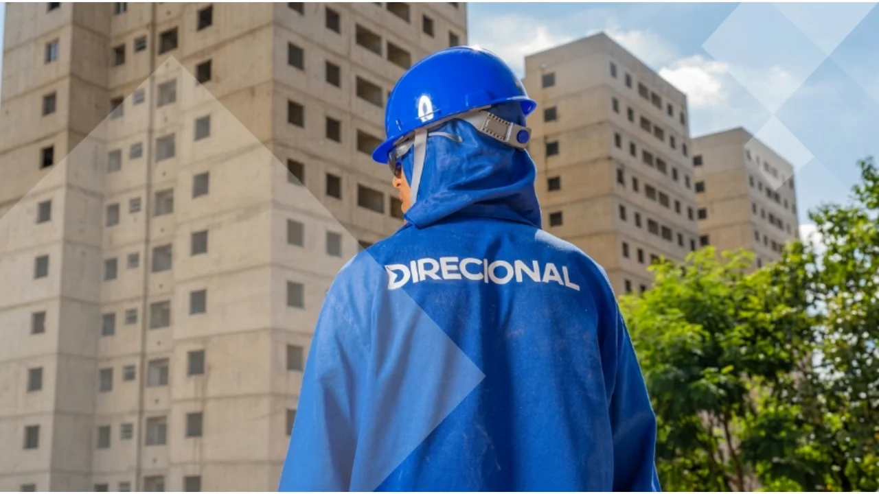 Operário com uniforme da Direcional observando edifícios em construção, ilustrando a desvalorização das ações na pauta Direcional cai.
