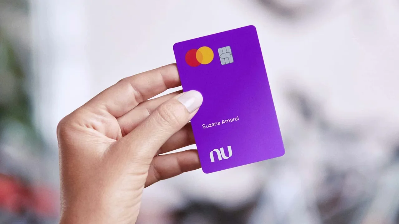 Mão feminina segurando o cartão de crédito roxo do Nubank com a marca Nu em destaque.