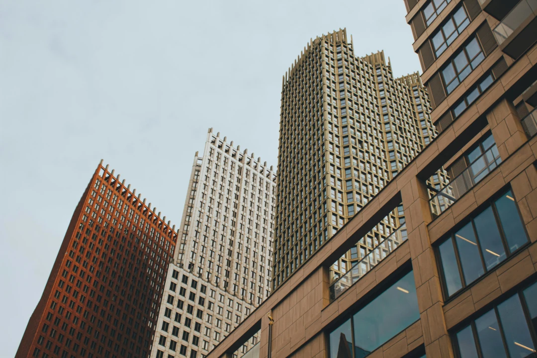 Fachadas de edifícios corporativos de grande porte em centro urbano, com arranha-céus modernos vistos de baixo para cima e céu claro ao fundo
