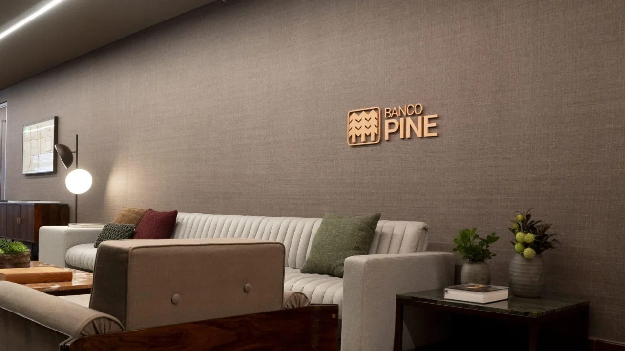 Área de espera de escritório corporativo do Banco Pine com sofá, poltrona e logotipo da empresa na parede.