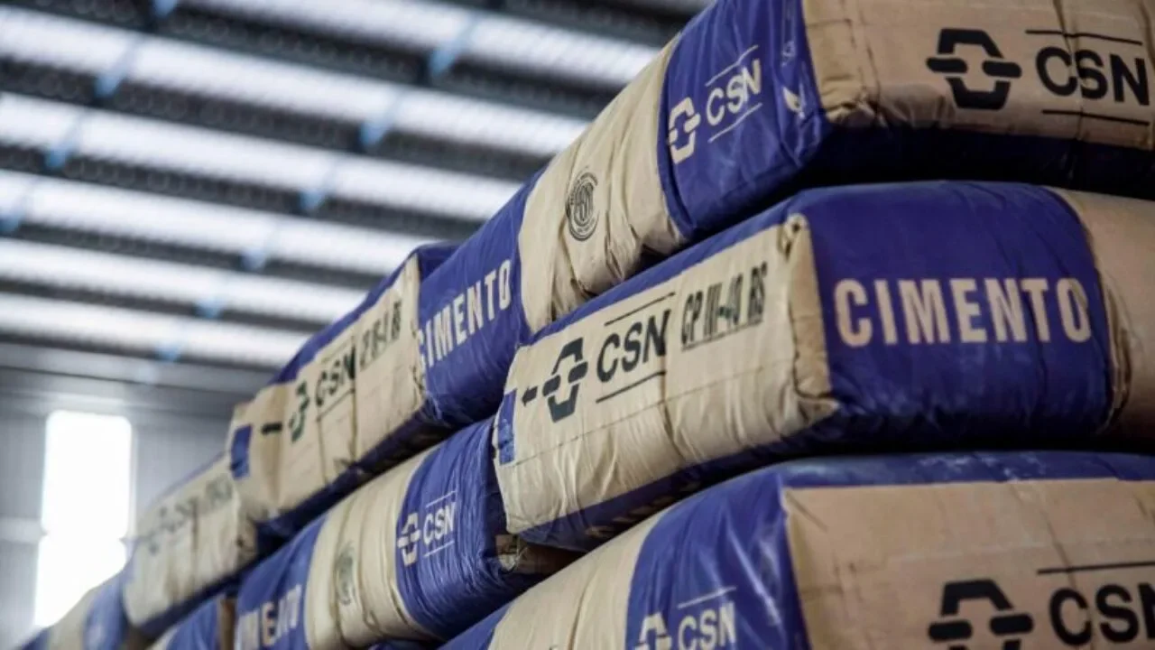 Sacos de cimento embalados com a marca CSN Cimentos empilhados em galpão logístico industrial.