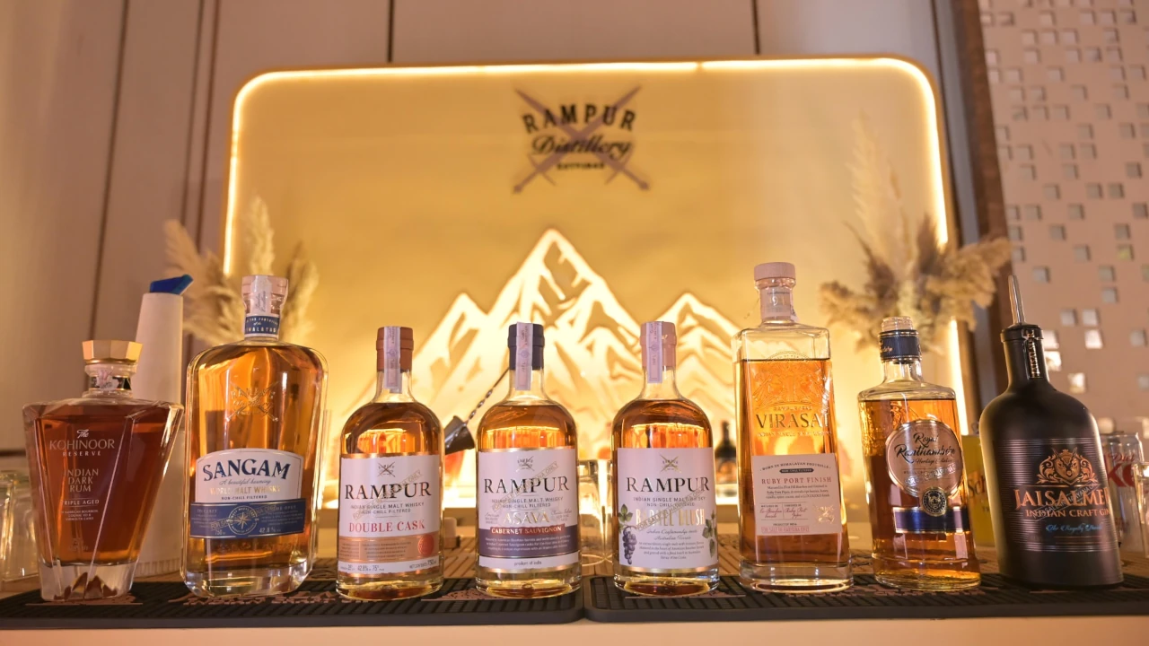 Garrafas de destilados premium da Radico Khaitan expostas sobre um balcão, incluindo os rótulos Jaisalmer, Rampur, Sangam e Kohinoor, diante de um painel iluminado com a marca Rampur Distillery ao fundo