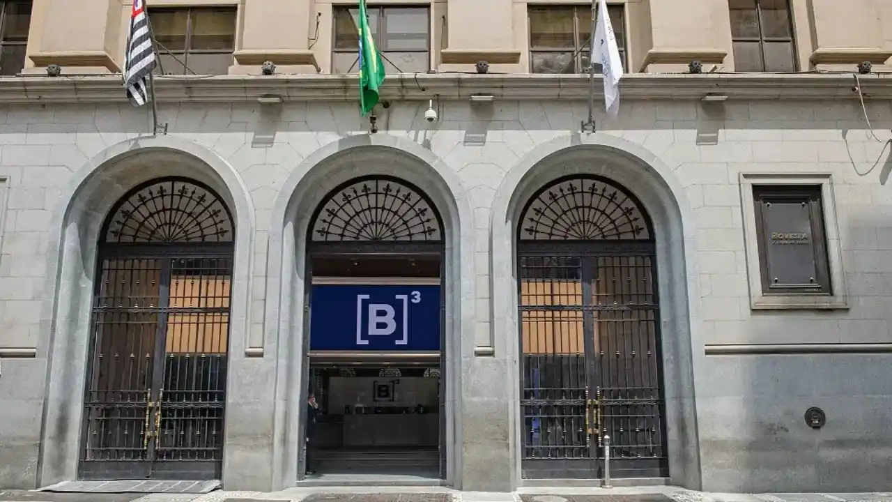 Fachada do prédio da B3, a Bolsa de Valores do Brasil, com destaque para a porta principal e as bandeiras de São Paulo e do Brasil, ilustrando o aumento do volume financeiro em ações.