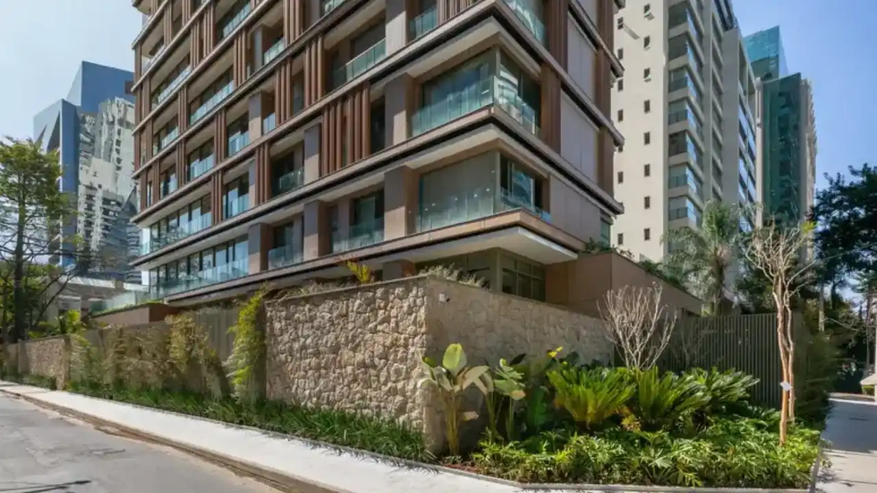 Fachada de empreendimento imobiliário residencial de alto padrão da Helbor, com varandas de vidro, acabamento moderno e paisagismo na calçada com muro de pedras no bairro Itaim Bibi, São Paulo.