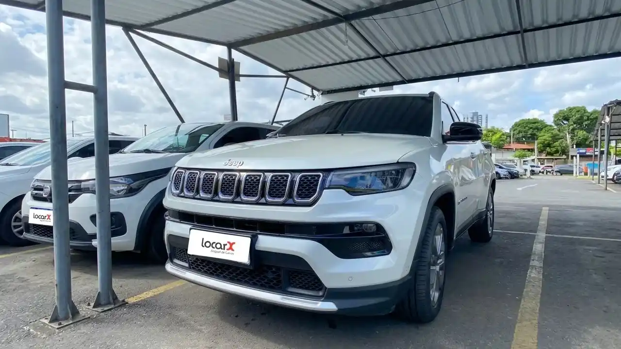 Veículo Jeep de cor branca estacionado sob cobertura na garagem da LocarX com identificação da marca na placa, ao lado de outros carros da frota de locação.