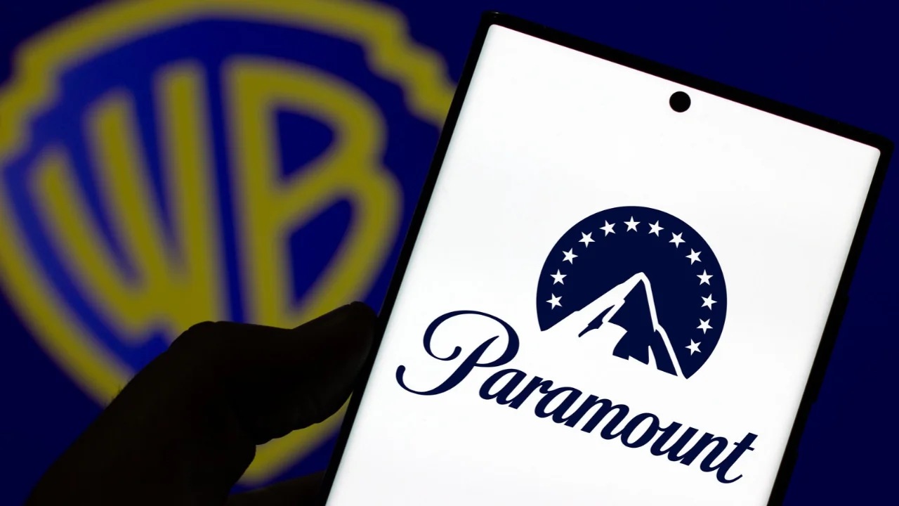 Smartphone exibe a logo da Paramount em frente ao símbolo da Warner Bros. em matéria sobre a compra de US$ 110 bilhões.