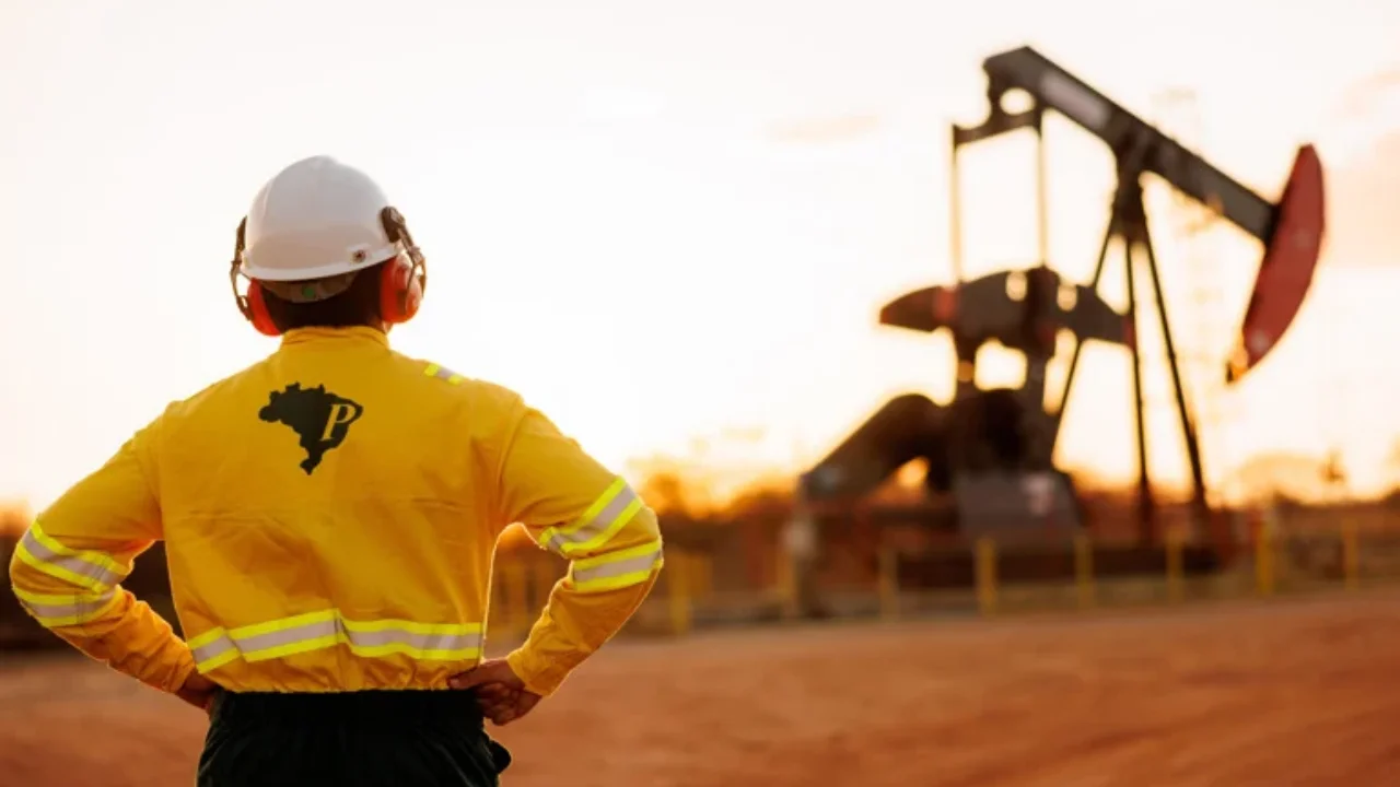 Funcionário da PetroReconcavo diante de poço terrestre de petróleo ao pôr do sol em matéria sobre a menor produção de 2026.