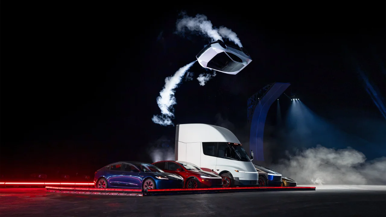 Carro elétrico Tesla Roadster prateado executando uma manobra aérea e liberando fumaça com propulsores sobre outros veículos da Tesla e um caminhão Tesla Semi em um palco iluminado à noite.