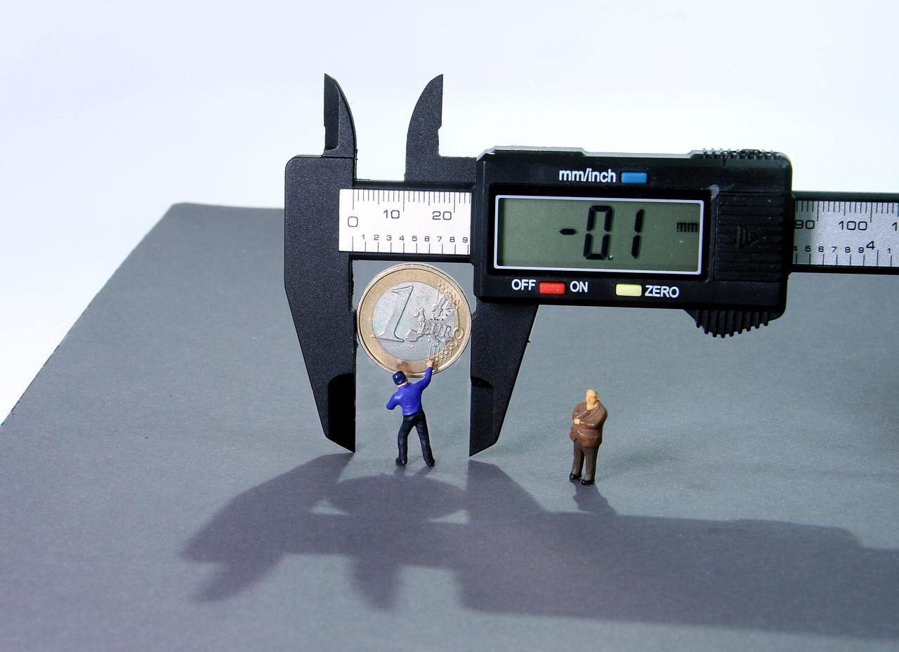 Imagem mostra uma moeda sendo pressionada e medida por ferramenta de medição, ilustrando a inflação.