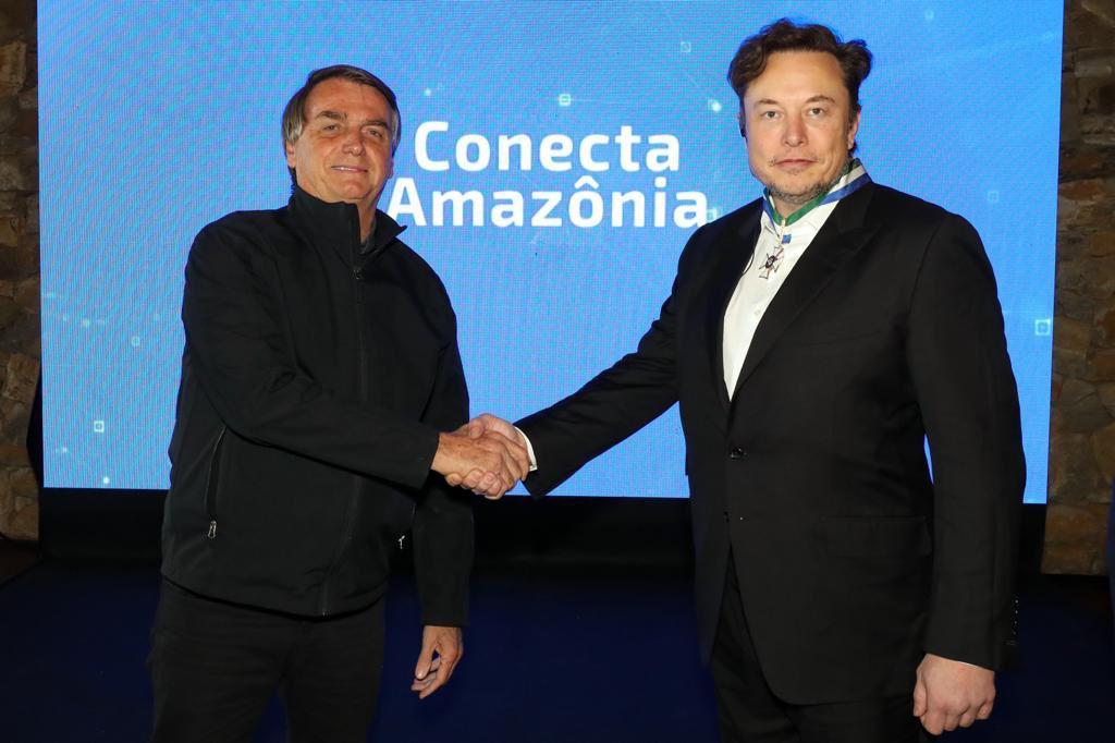 Iagem mostra Jair Bolsonaro à esquerda dando a mão para Elon Musk, à direita.