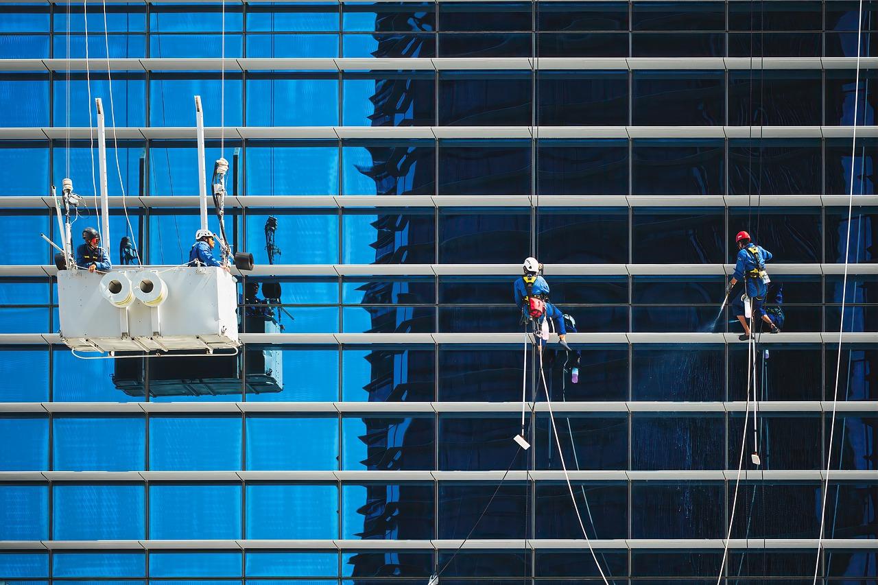 Imagem mostra trabalhadores limpando os vidros de um edifício de escritórios.