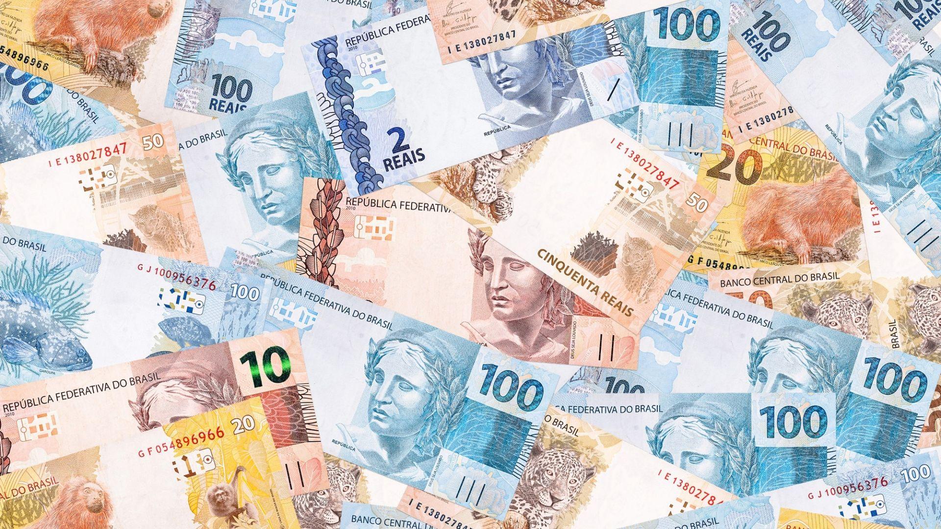 A imagem mostra diversas notas de dinheiro sob uma mesa.