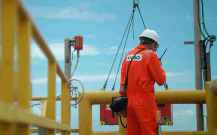 Imagem mostra plataforma da PetroRio (PRIO3) com funcionário de roupa laranja da empresa, de costas, com o mar ao fundo