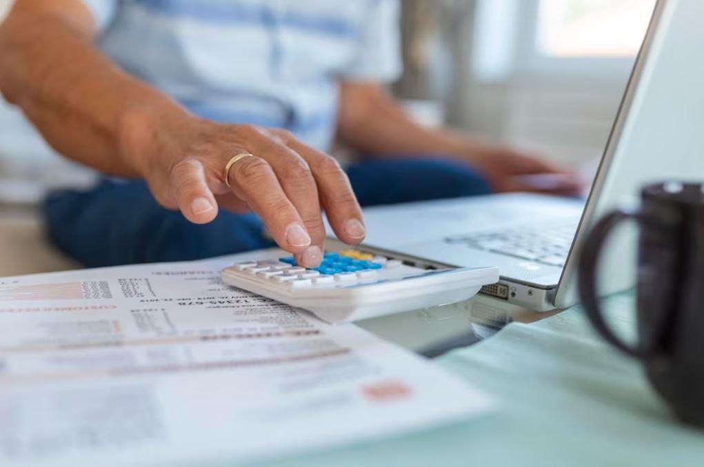 imposto de renda: foto de homem à calculadora e ao computador, fazendo contas