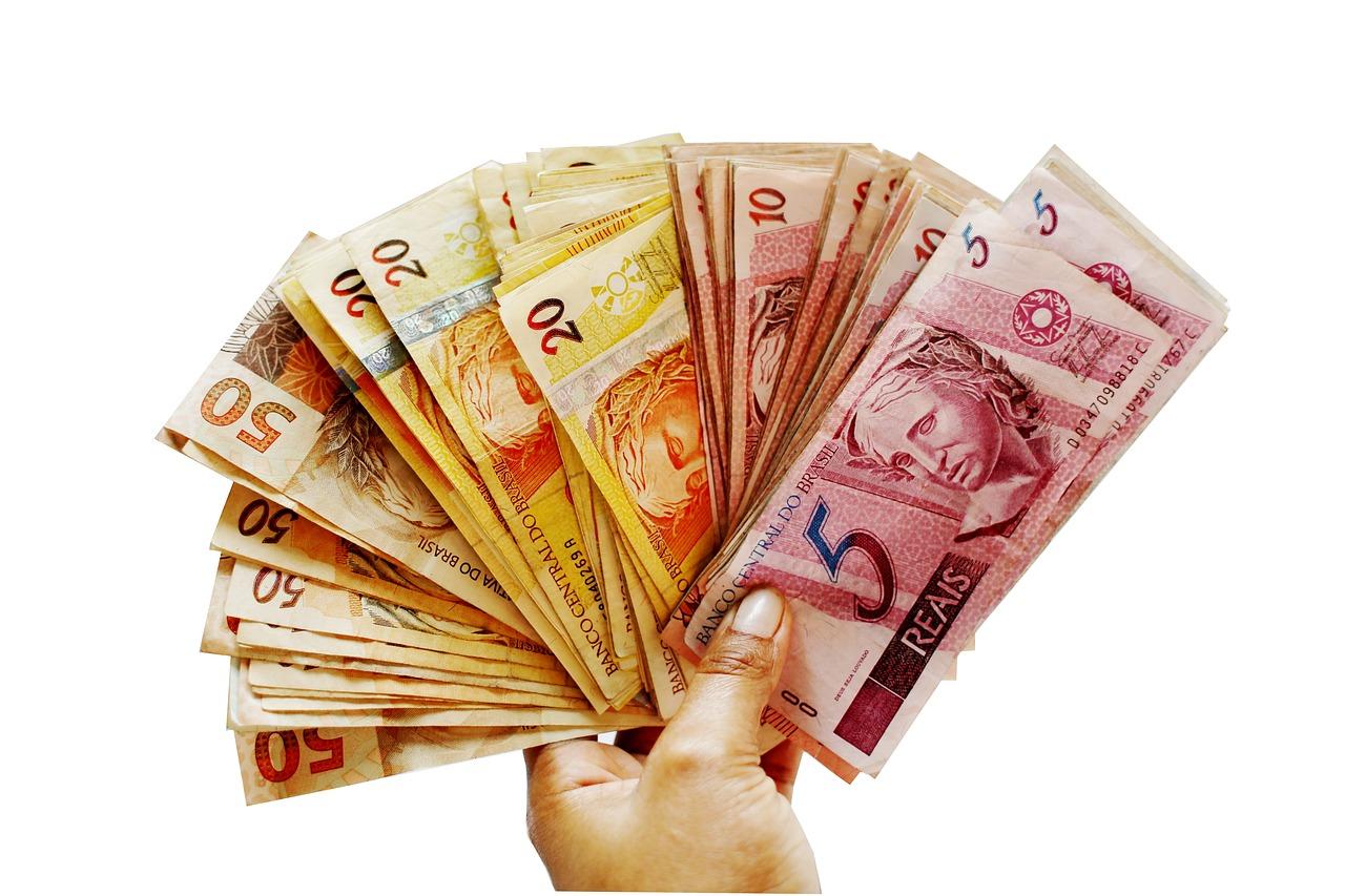 Imagem mostra uma mão segurando um punhado de dinheiro.