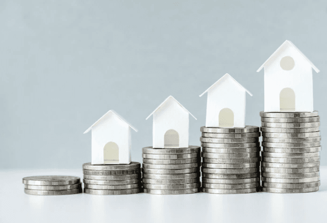 Foto de pilhas de moedas e casinhas de papel: fundos imobiliários e expectativa de retorno dos FIIs