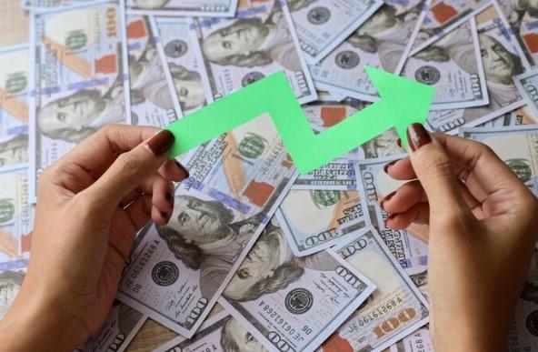 hora de dolarizar patrimônio com renda fixa: mulher segura seta para cima em meio a notas de dólares