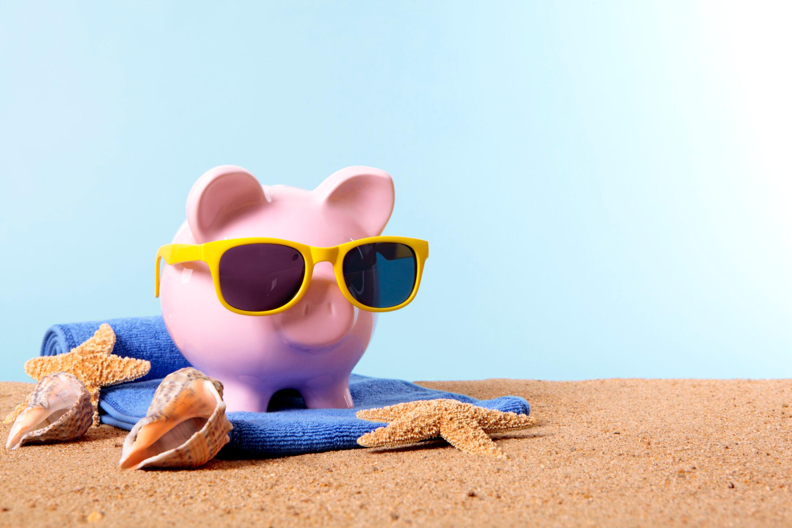 Pink piggy bank on a beach with sunglasses and beach towel. Liberdade Financeira