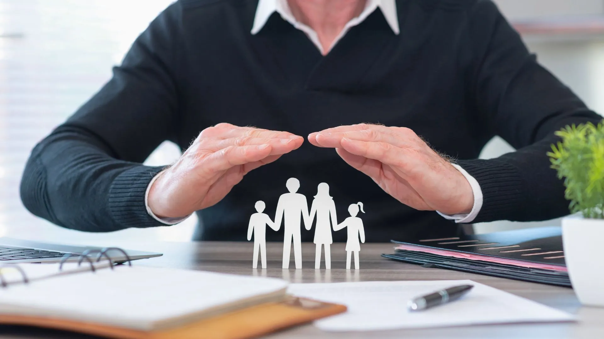 Homem protege simbolicamente uma família com as mãos, representando a segurança oferecida pelo seguro de vida.