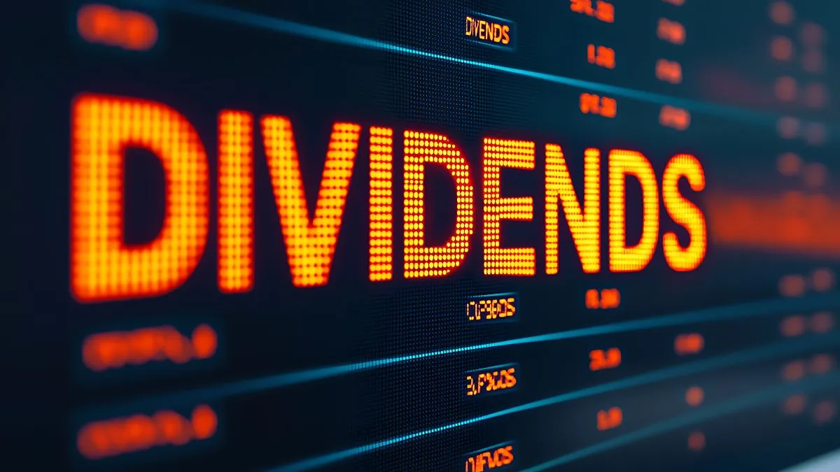 A palavra "DIVIDENDS" iluminada em laranja em um painel digital, com números e códigos de ações no fundo, sugerindo o conceito de lucros e investimentos em ações